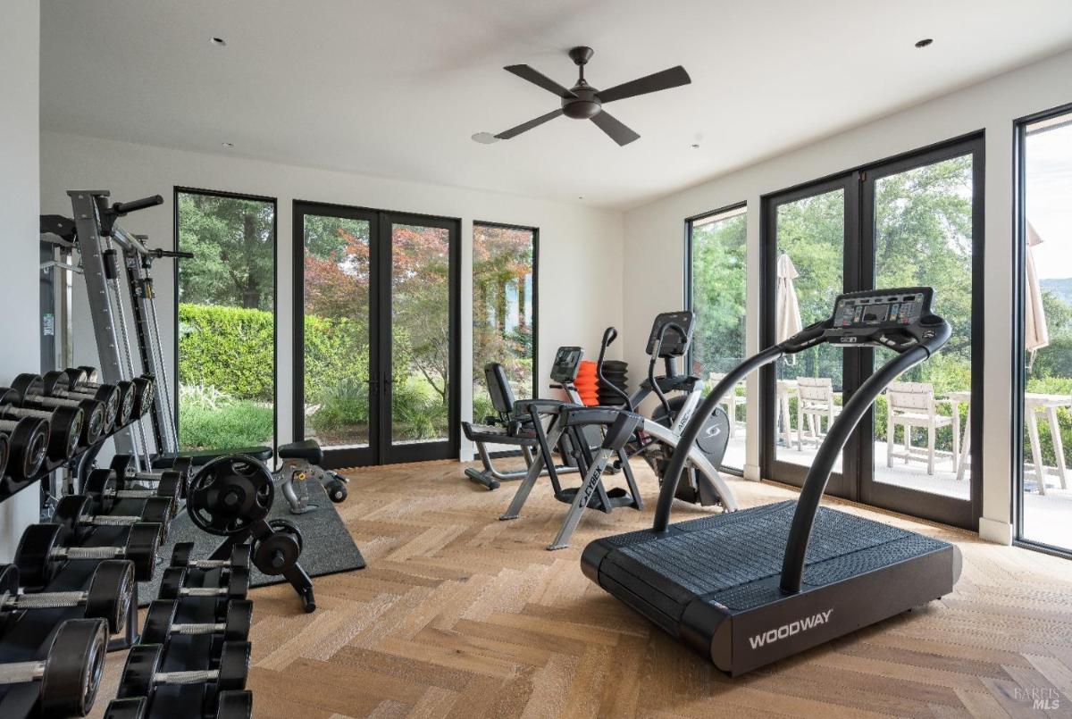 Home gym with exercise equipment, large windows, and glass doors leading to a patio.