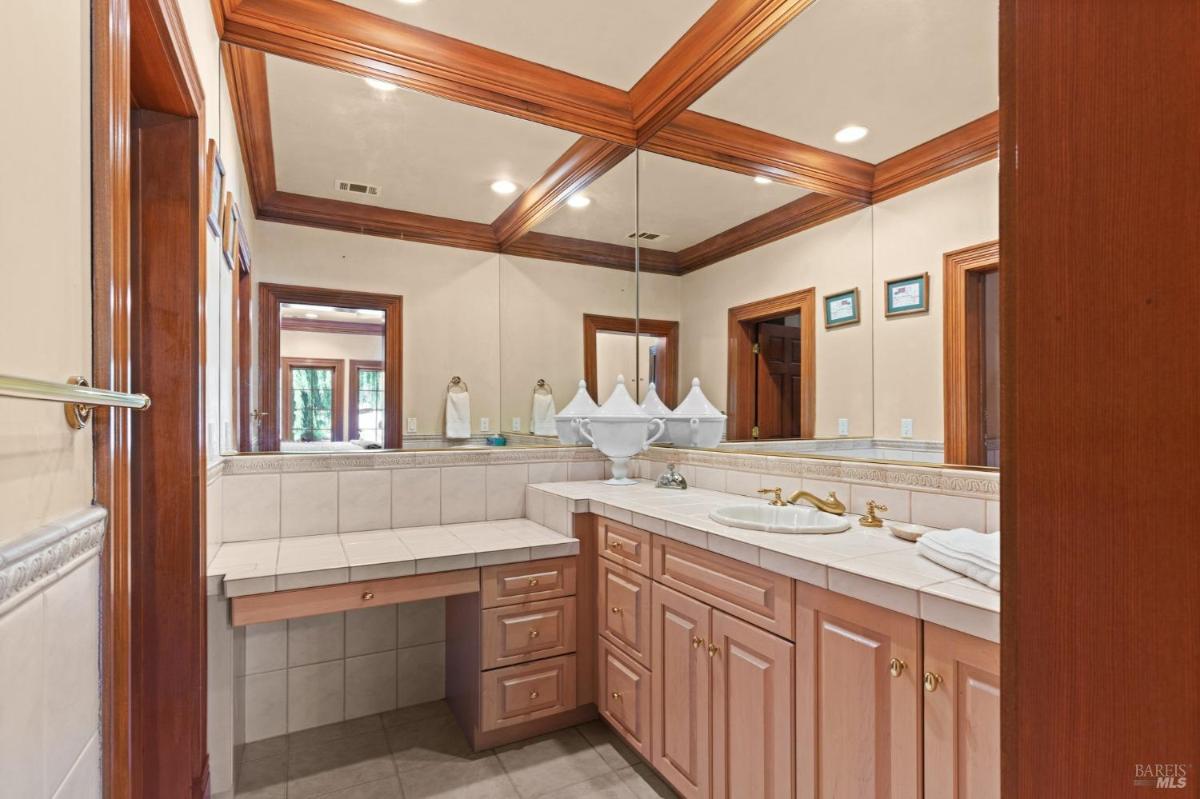 Corner bathroom with dual sinks, tile countertops, and framed mirrors.