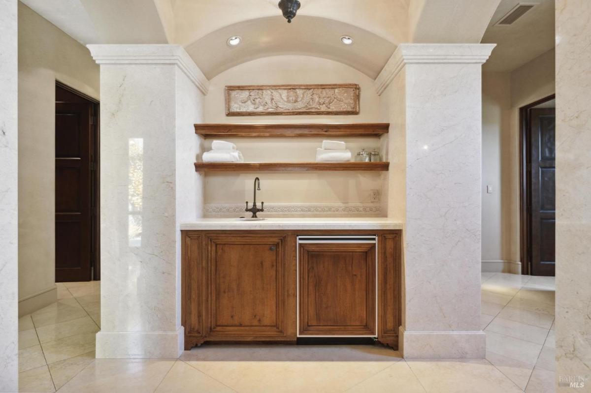 bathroom area showcasing a wooden shelf with neatly stacked towels, a small sink, and a compact cabinet below.