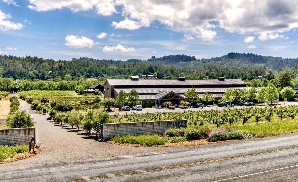 Vineyard entrance with a building surrounded by greenery and hills in the background.