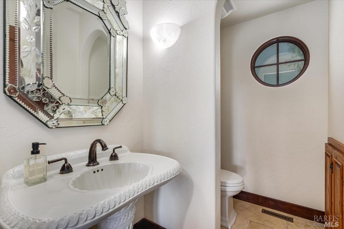 A small powder room with a pedestal sink and decorative mirror.