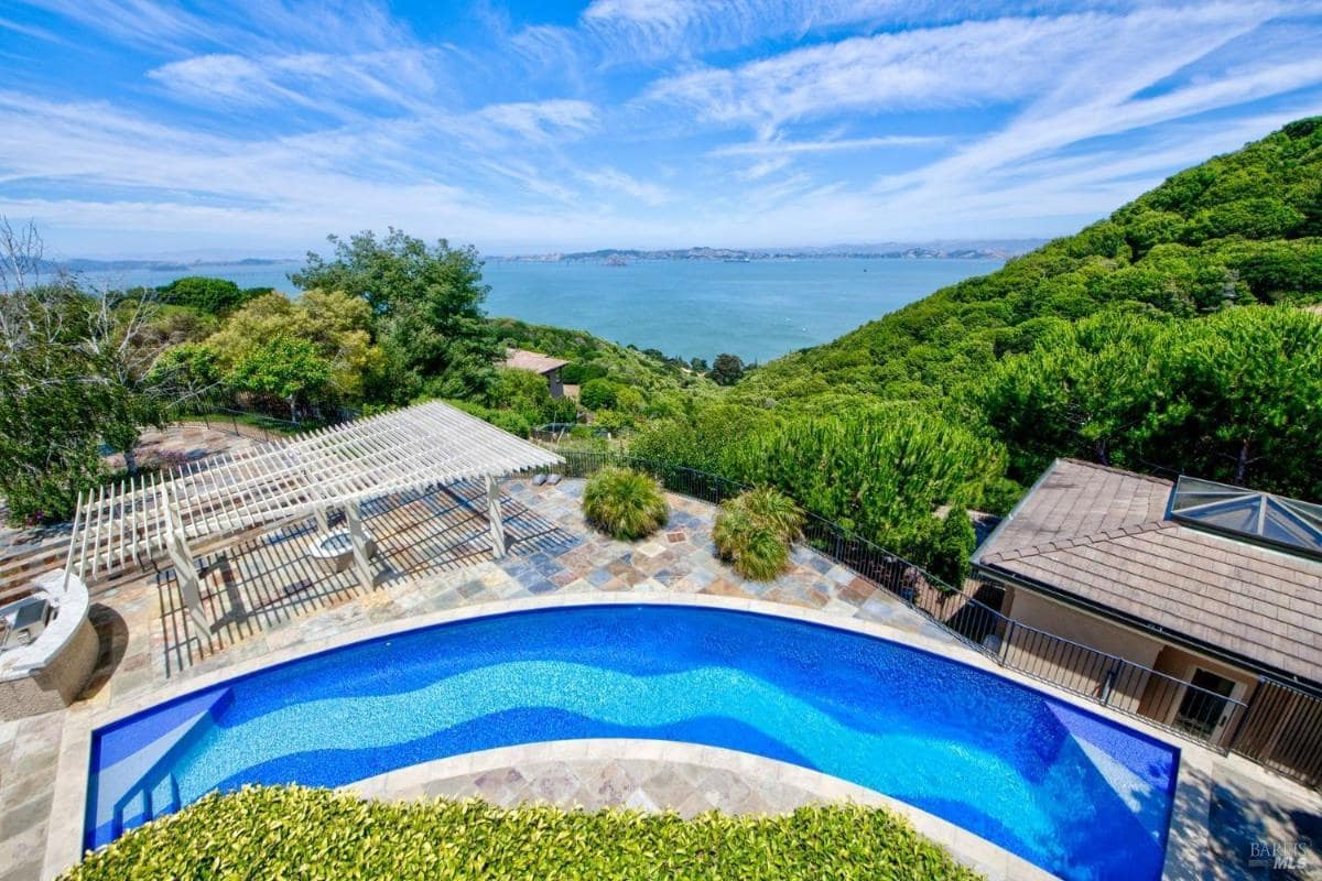 Outdoor pool area with a pergola and surrounding greenery.