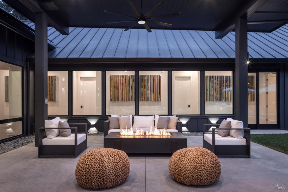 Terrace seating area with a central fire pit, modern furniture, and decorative poufs under a covered patio.