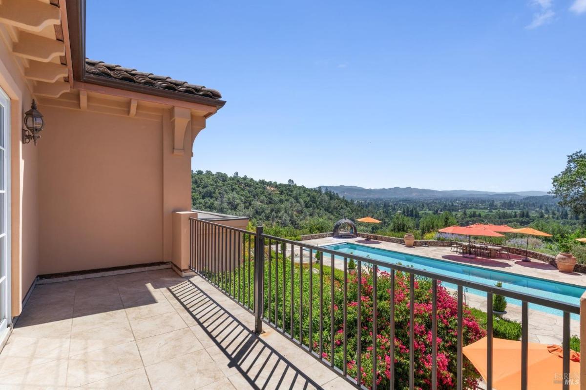 Private balcony with tiled flooring, overlooking a pool, hills, and lush greenery.