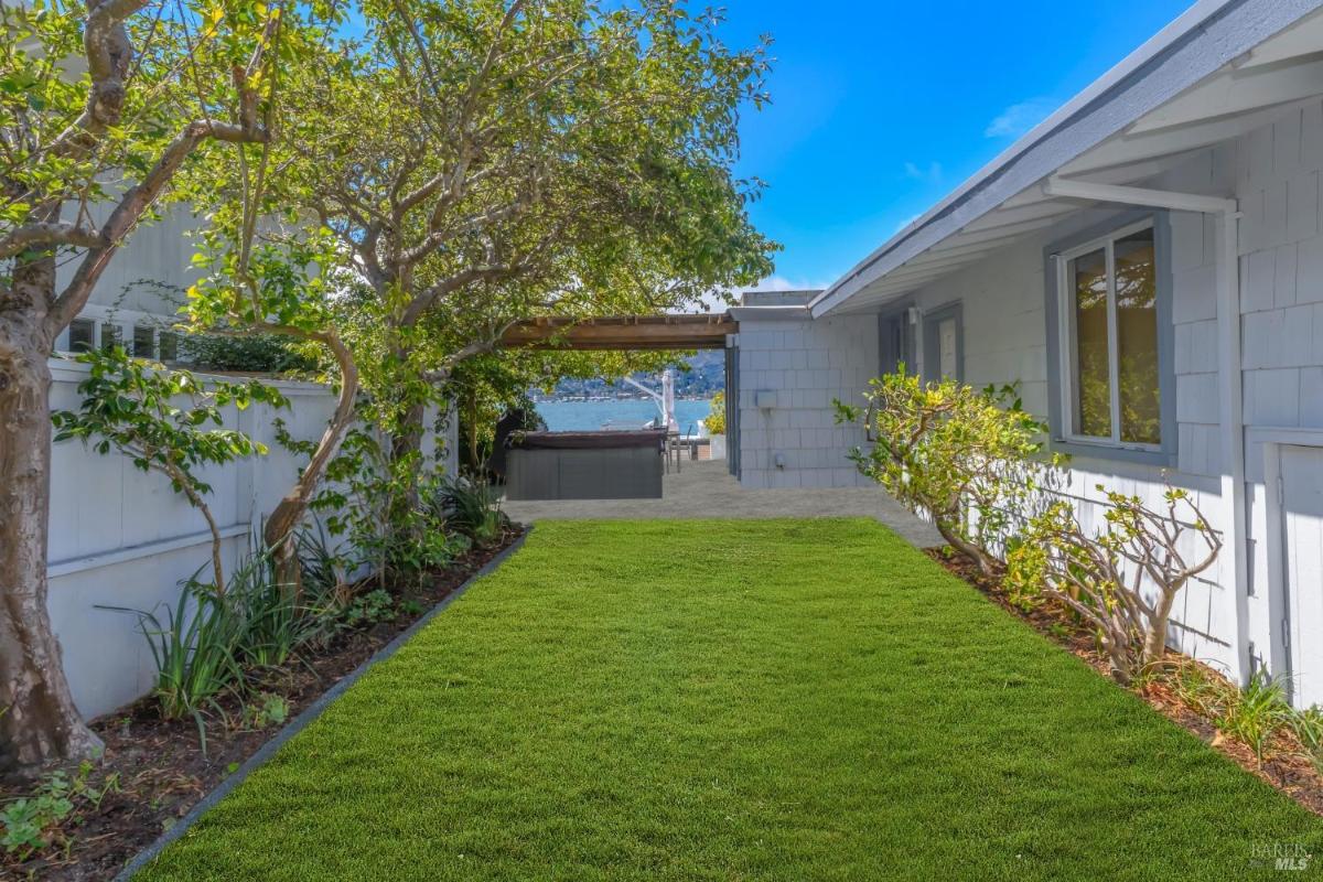 A grassy backyard pathway leading to an outdoor area with a hot tub and seating, overlooking the water.