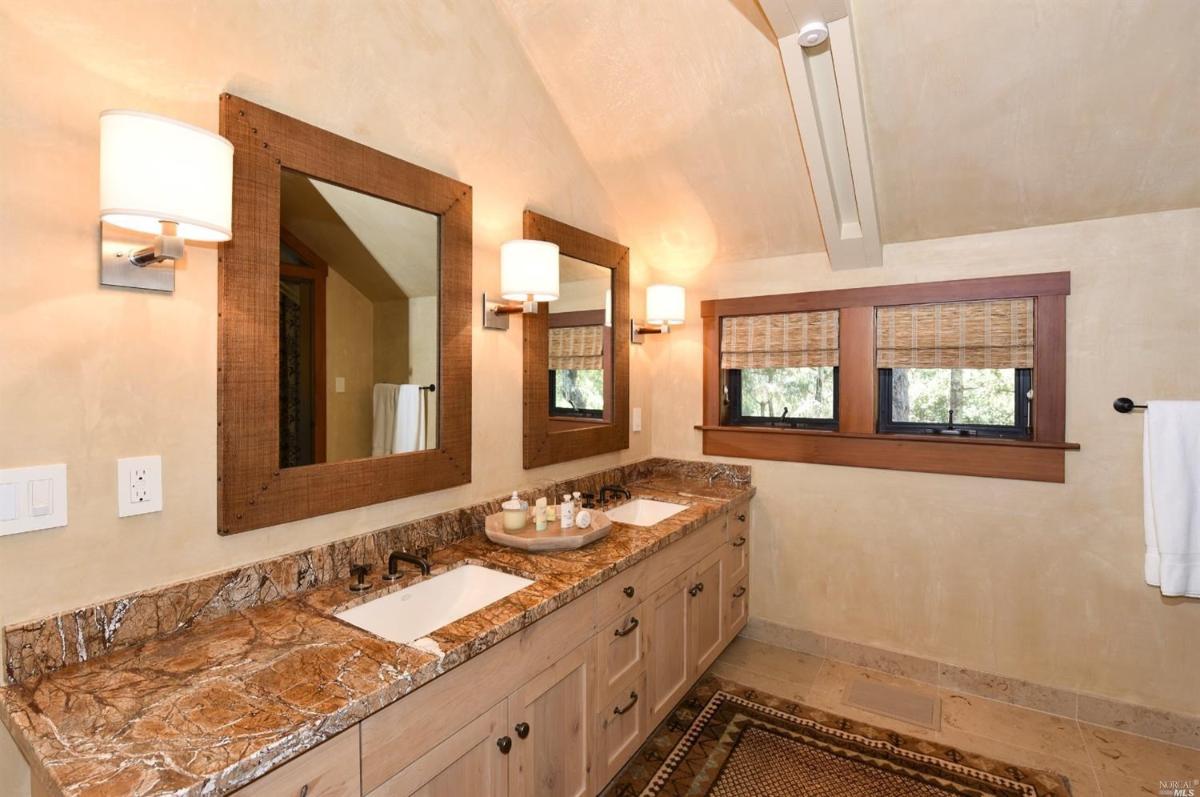 A bathroom with double sinks, wooden accents, and a glass-enclosed shower.