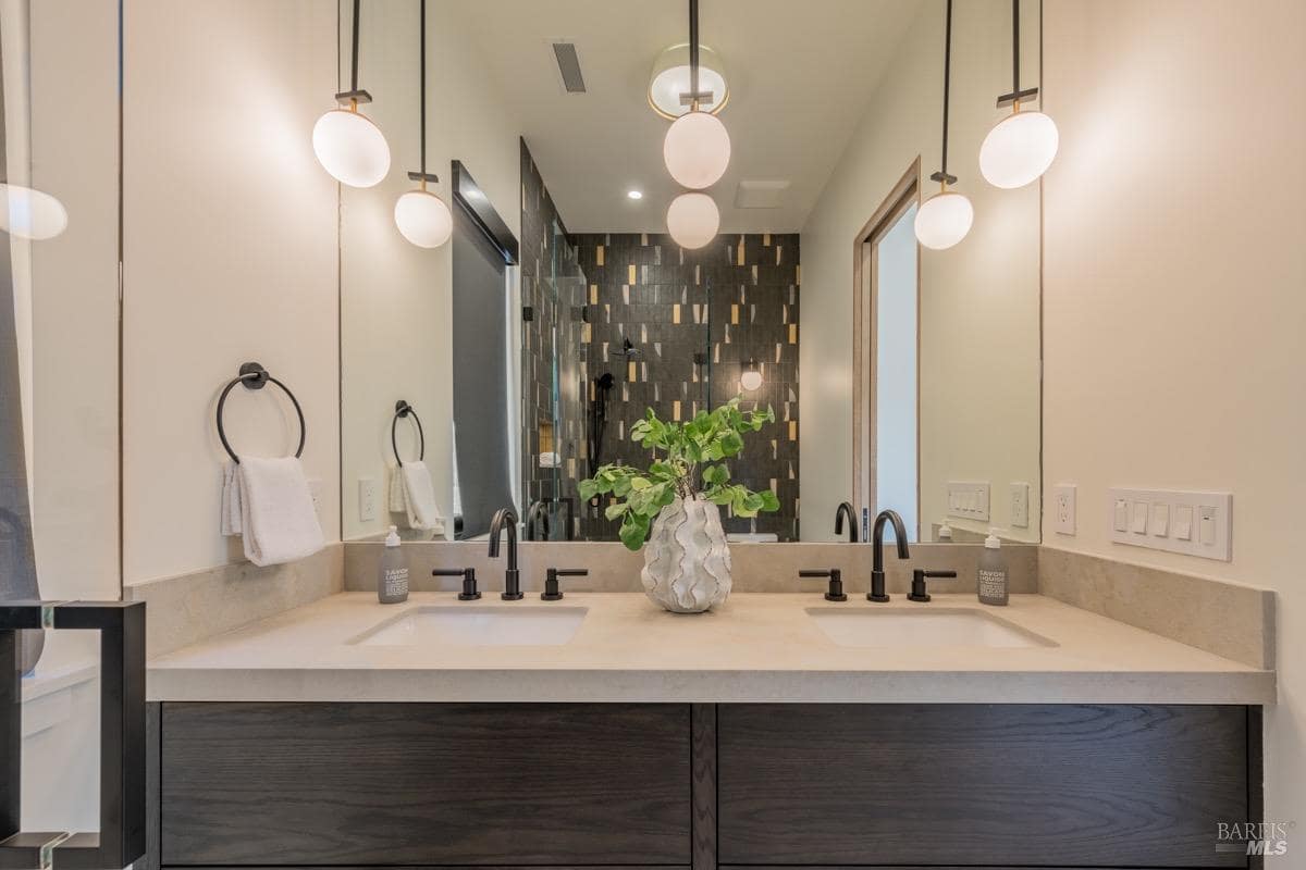 A bathroom with a double vanity, modern pendant lights, and a dark-tiled walk-in shower.