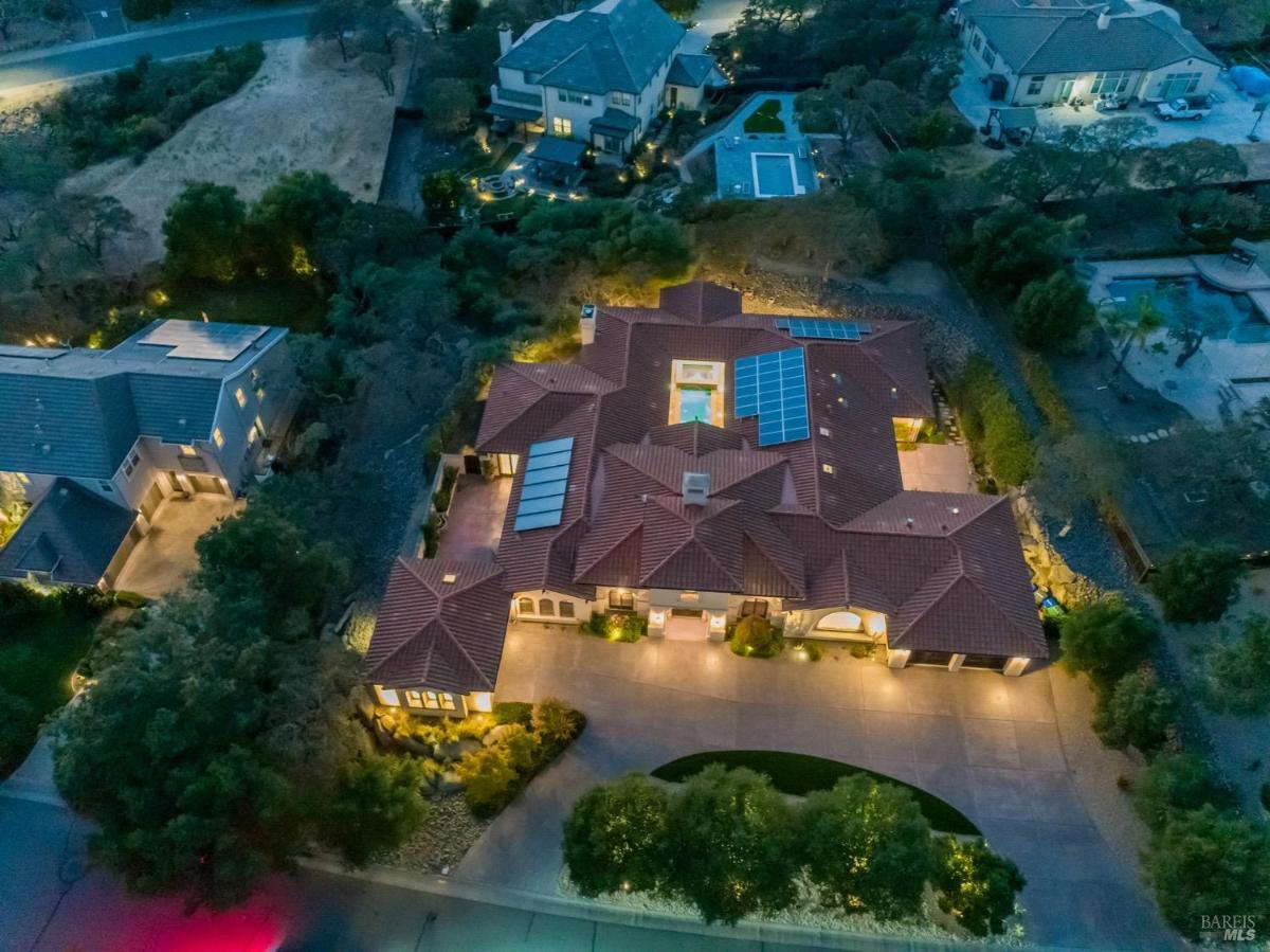 An aerial view of a large house with a tiled roof surrounded by trees and hills.