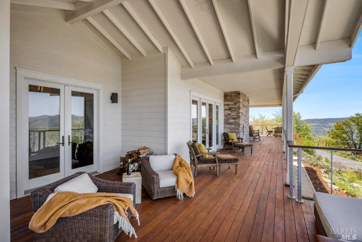 A porch with seating and a stack of firewood offers a view of the surrounding hills.