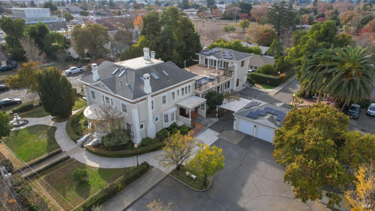 Aerial view of a house with landscaped gardens and adjacent buildings.