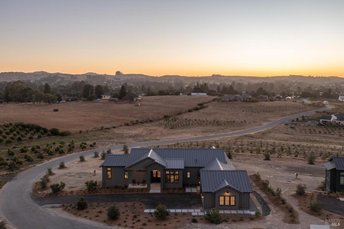 An aerial view of a modern house with a driveway and surrounding landscape at dusk.