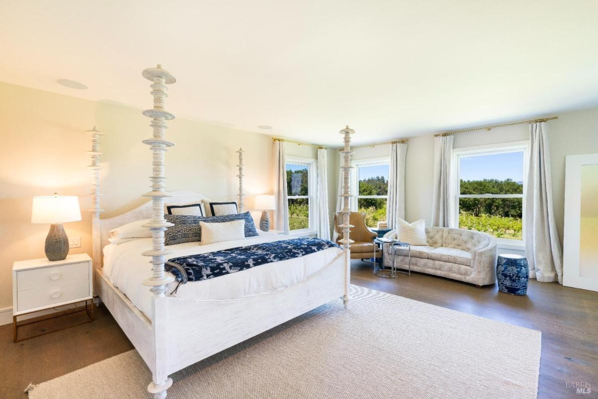 Bedroom with a four-poster bed, seating area, and multiple windows.