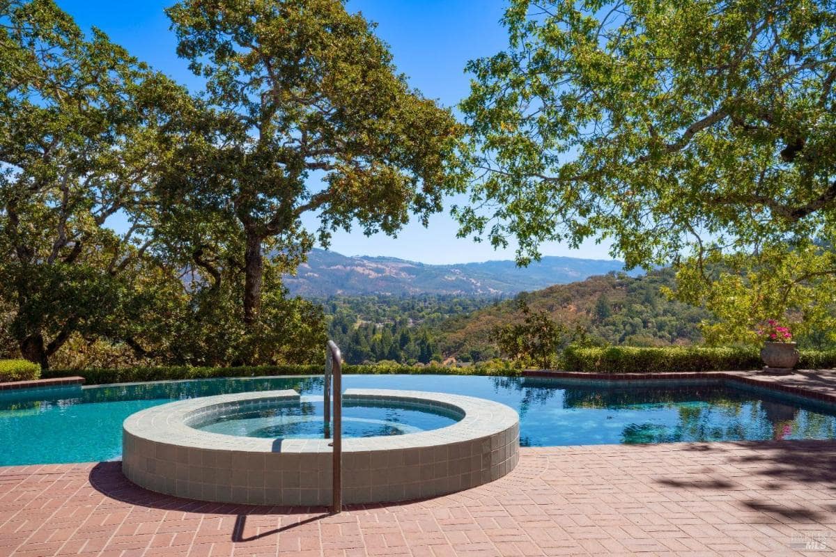 Outdoor hot tub and pool with trees and hills in the background.