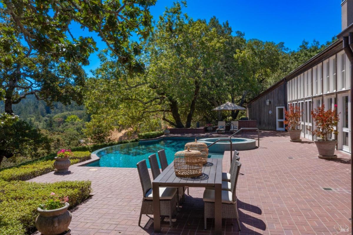 An outdoor patio with a dining table, pool, and surrounding greenery.