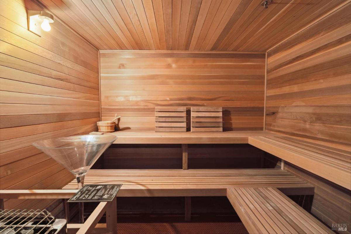 A wooden sauna interior featuring bench seating, a heater, and a bucket for water.