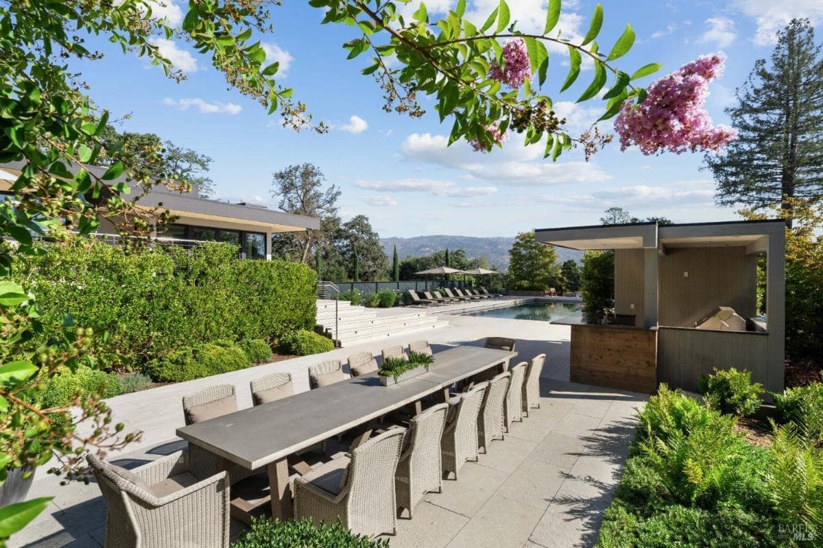 Outdoor dining table with seating and an adjacent pool area featuring lounge chairs and a pool house.