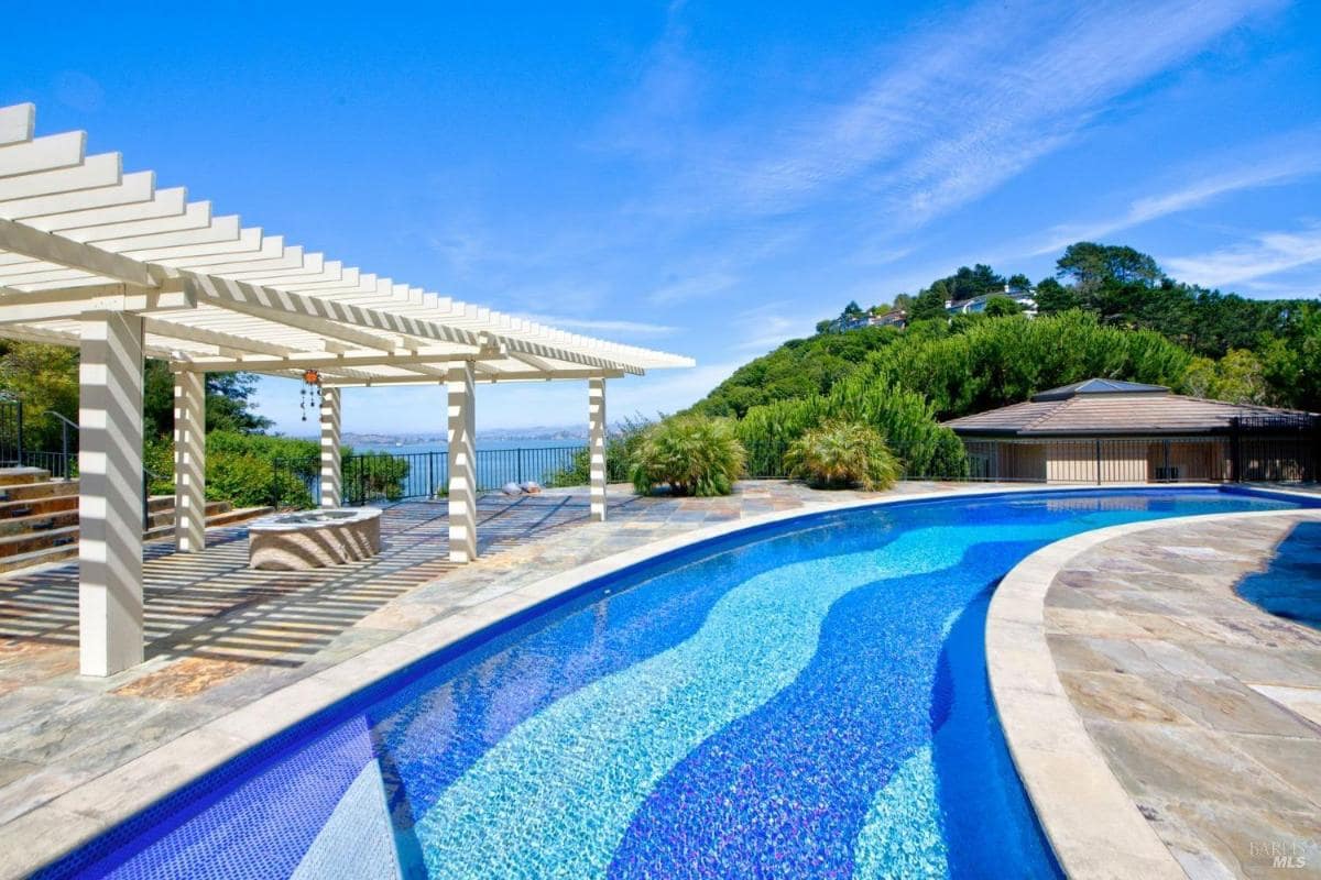 Outdoor pool area with a pergola and surrounding greenery.