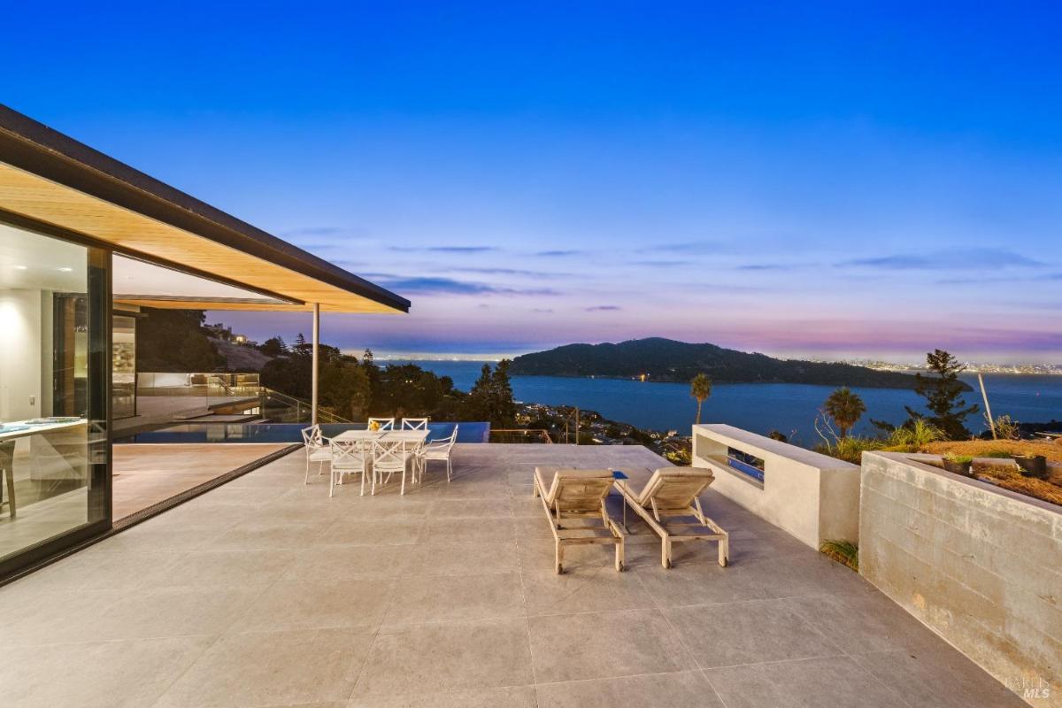 A patio with lounge chairs, a dining set, and an infinity pool overlooking the bay.