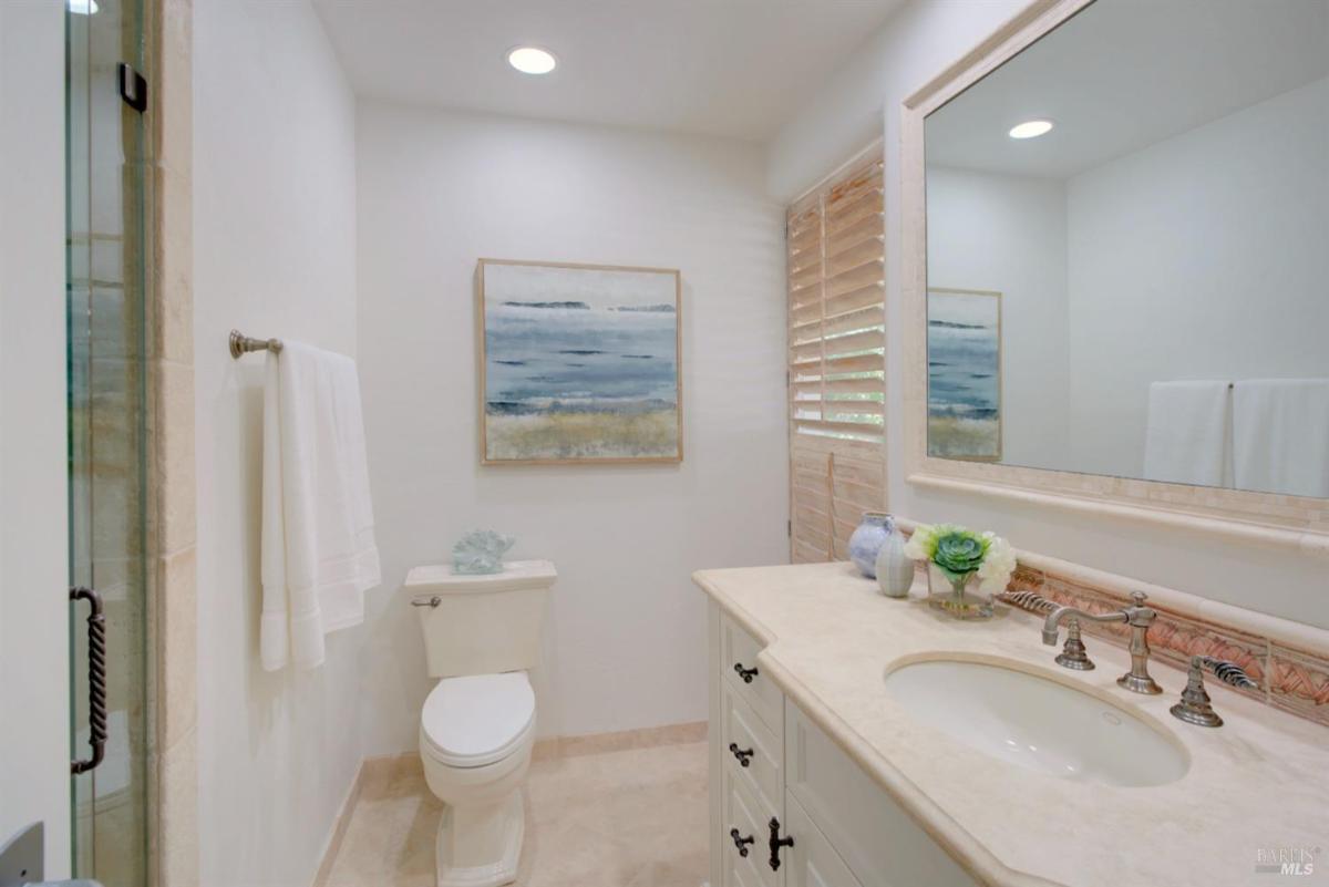 A bathroom with a single sink, wall-mounted mirror, and a toilet next to a shower.