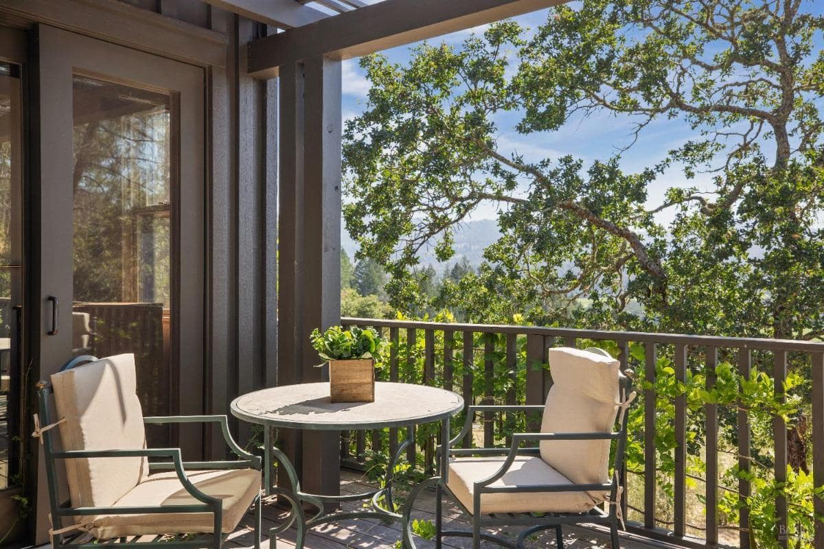 A balcony with a small table, two chairs, and a forest view.