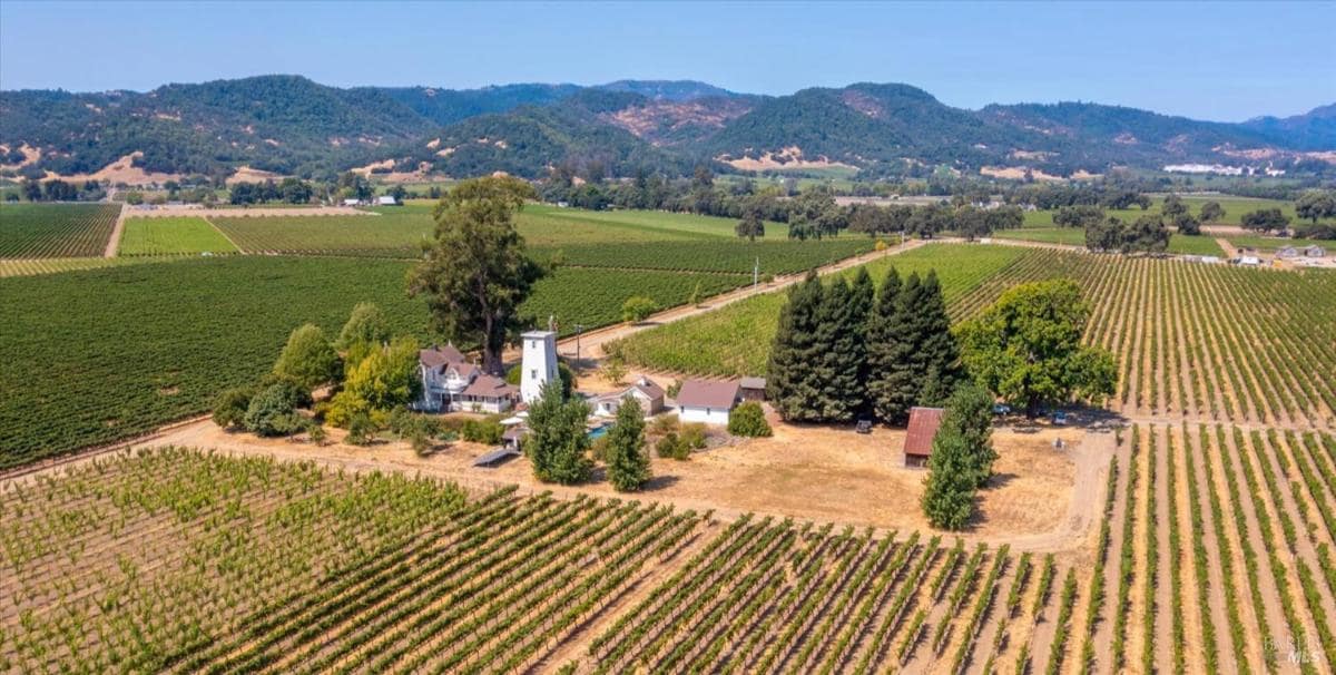 Aerial view showing expansive vineyards and hills, with a property featuring a white house and tower in the center.