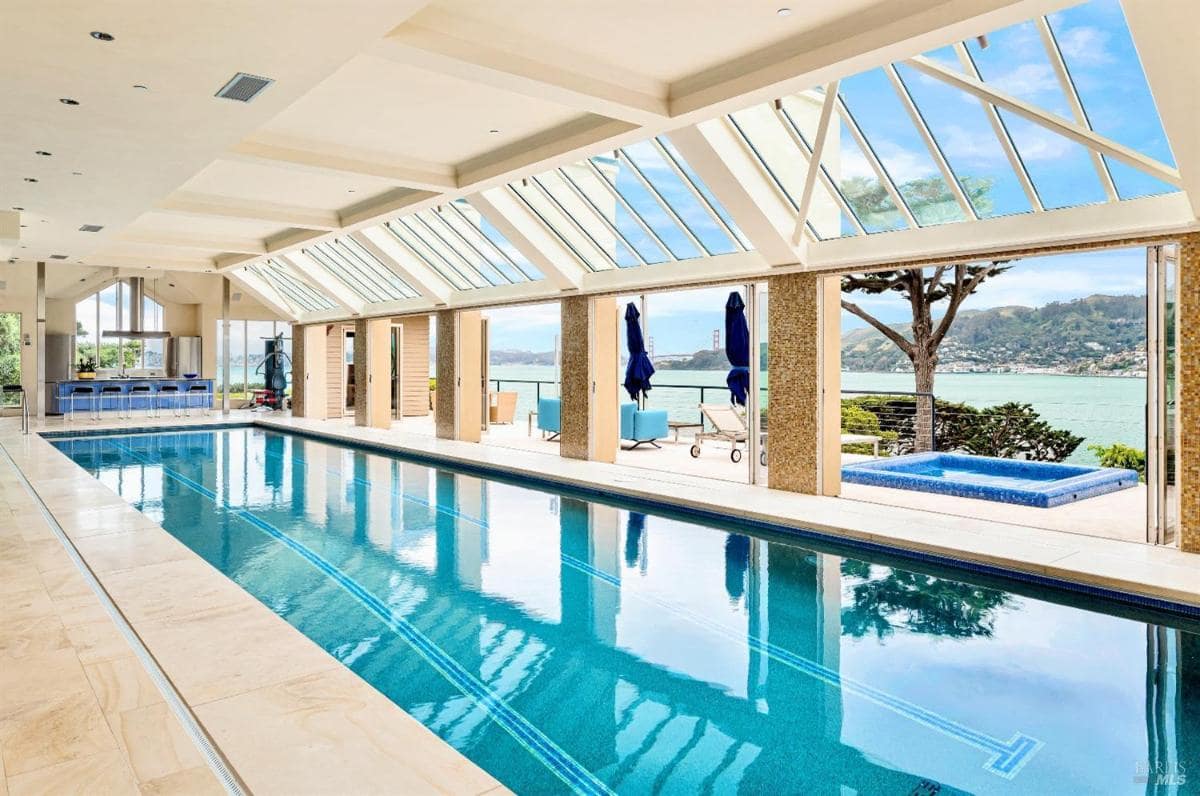 Large indoor swimming pool with a separate hot tub. The space opens to a deck overlooking panoramic water views.