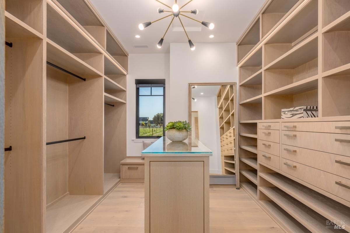 A spacious walk-in closet with built-in wooden shelves, a central island, and a large mirror.