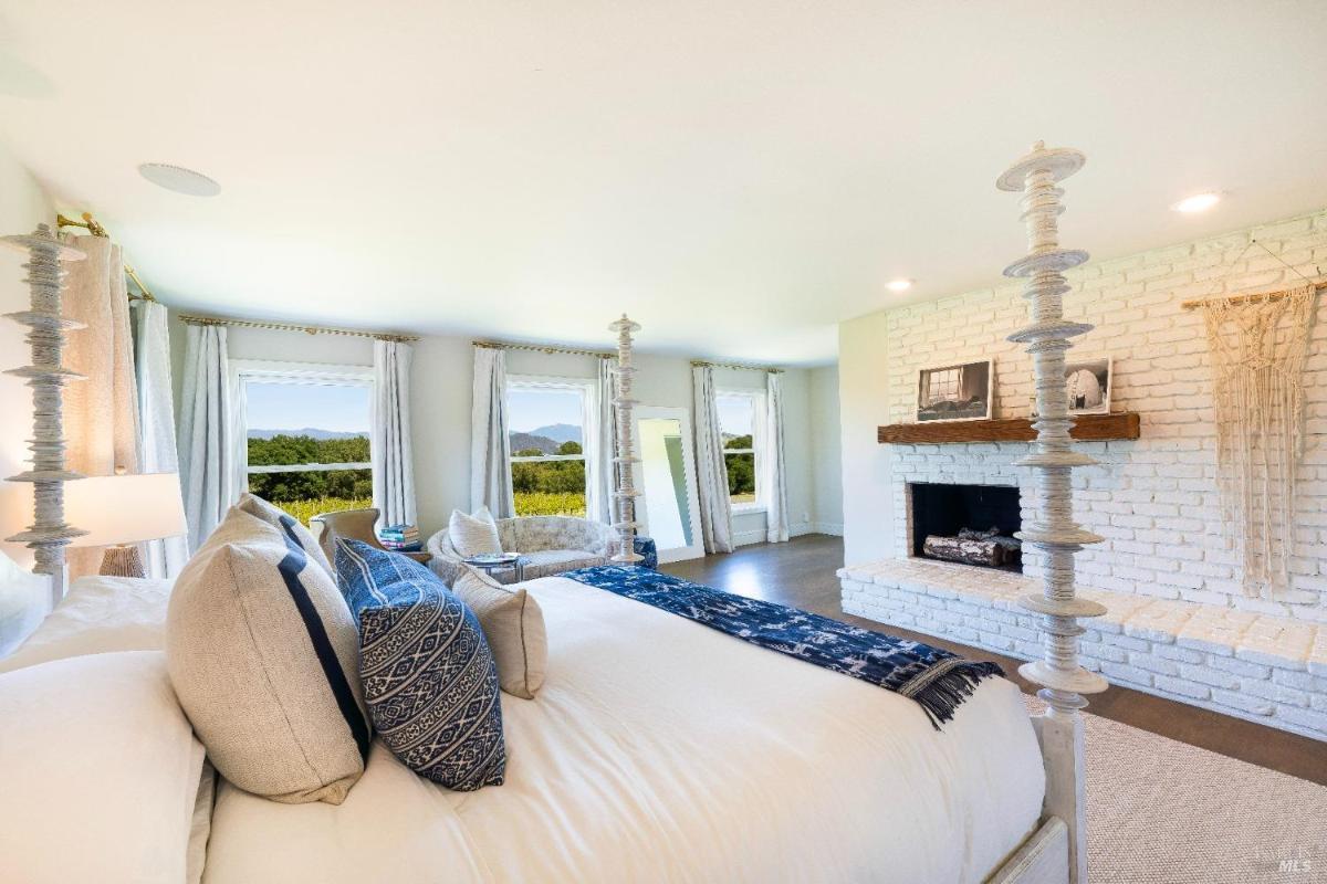 Bedroom with a fireplace, windows, and views of the outdoors.