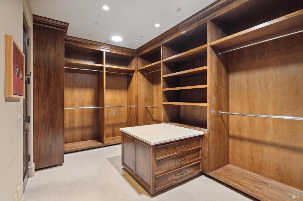 A spacious walk-in closet with wooden shelves, hanging rods, and a central island with drawers.