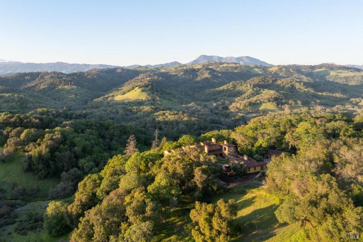 Aerial view of hills and a house nestled in the trees.