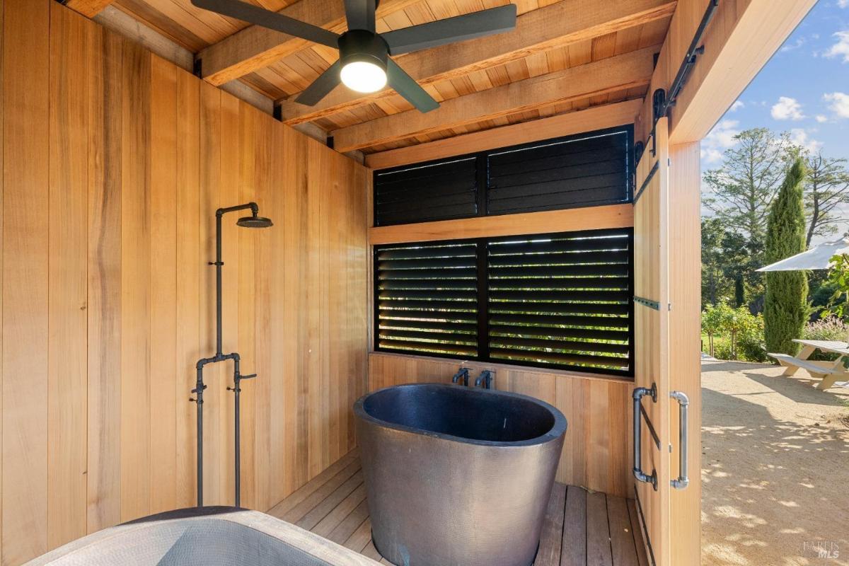 A covered wooden area with a black freestanding tub, a ceiling fan, and an outdoor shower.