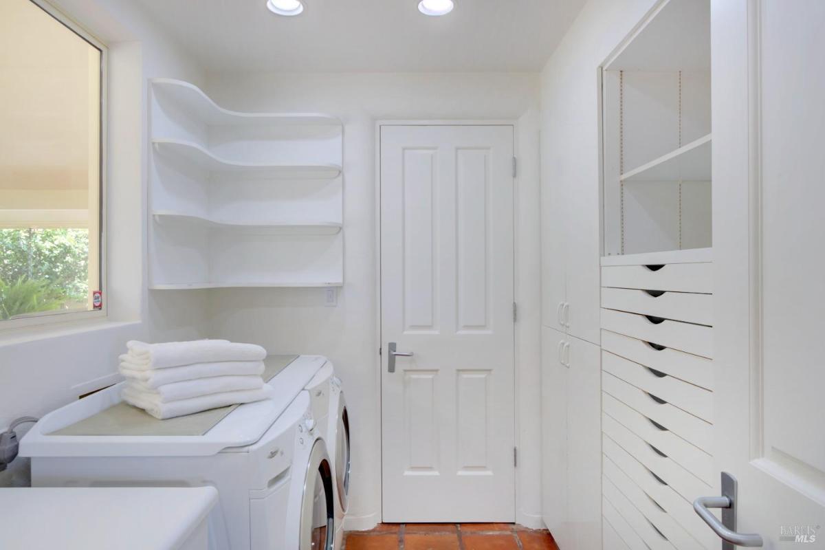 A laundry room with a washing machine, shelves, and a storage closet.