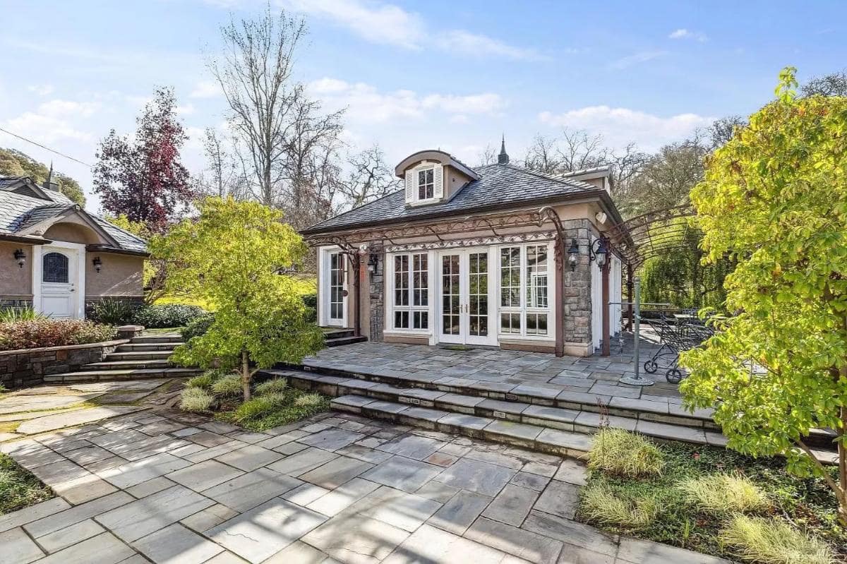 A stone-paved cottage featuring a single-story building with French doors and a decorative wrought iron frame along the exterior.