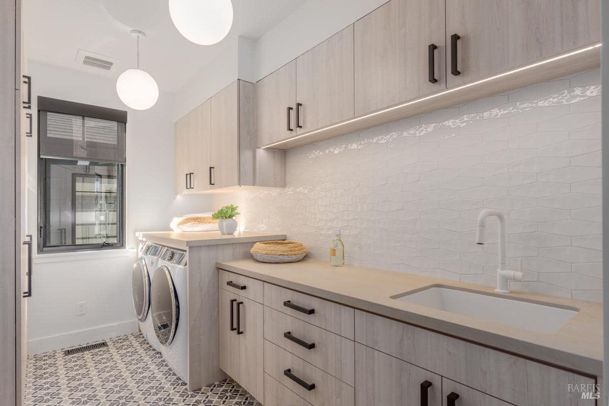 A functional laundry room with built-in cabinets, a countertop sink, and a washer-dryer setup.