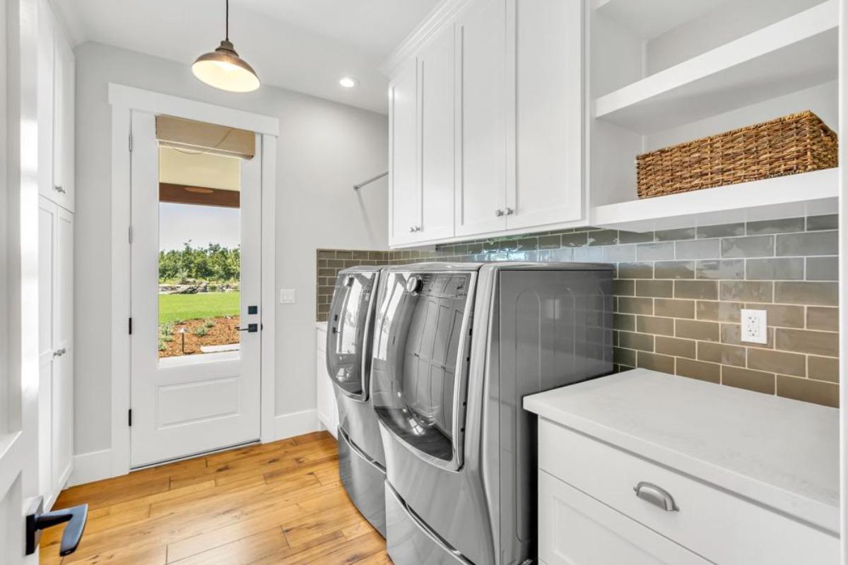 A laundry room with two gray washing machines, a countertop, and a door leading outside.