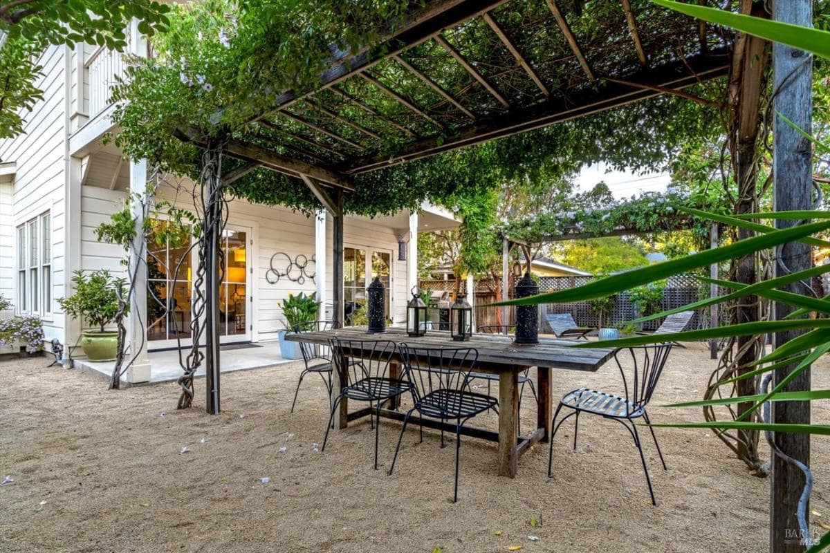 Outdoor dining area with wooden table and pergola covered in greenery