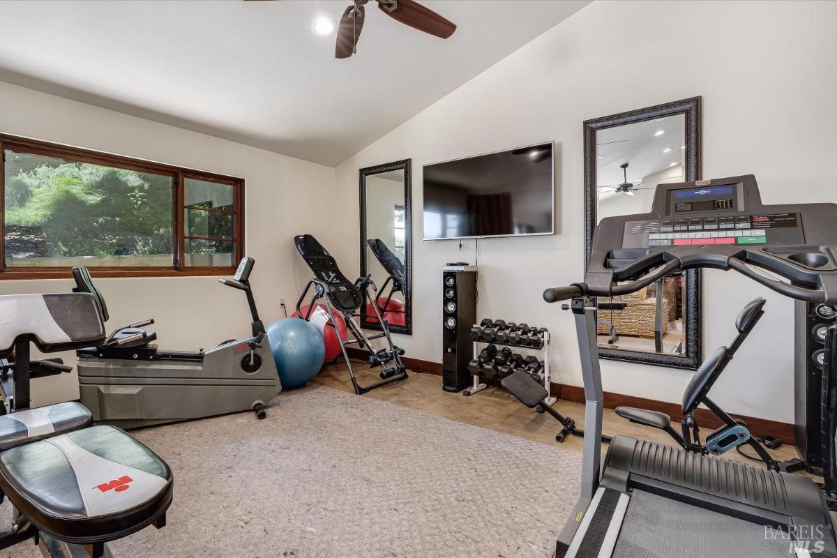 A home gym with exercise equipment, mirrors, and a wall-mounted television.