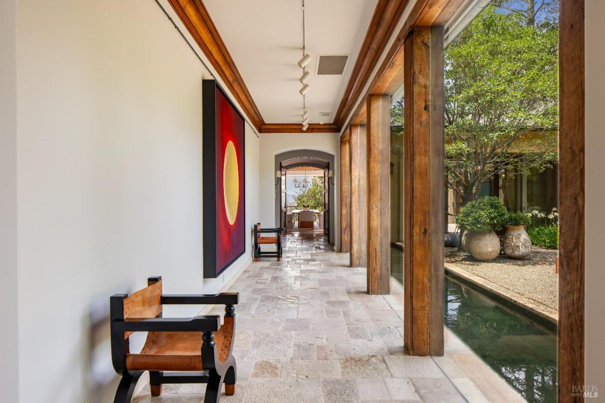 A hallway with glass walls and wooden beams, leading to an outdoor space.