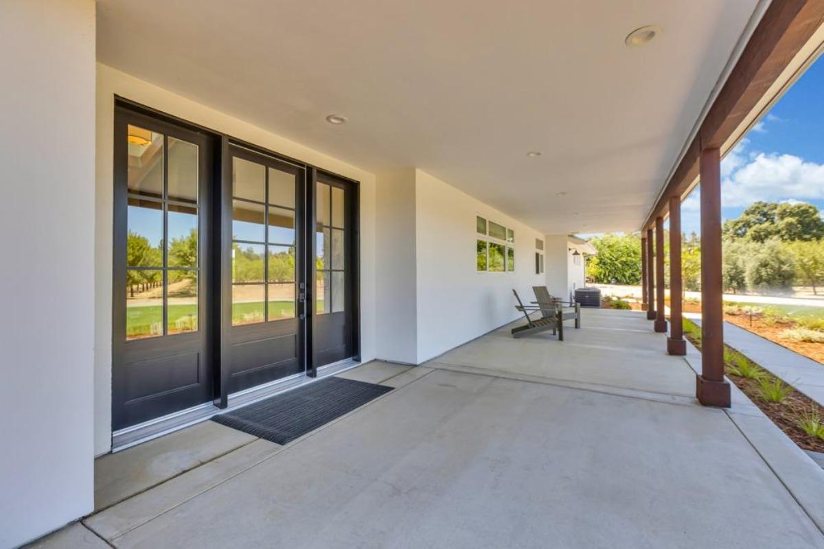 An outdoor entrance with double doors, a covered porch, and seating area overlooking a garden.