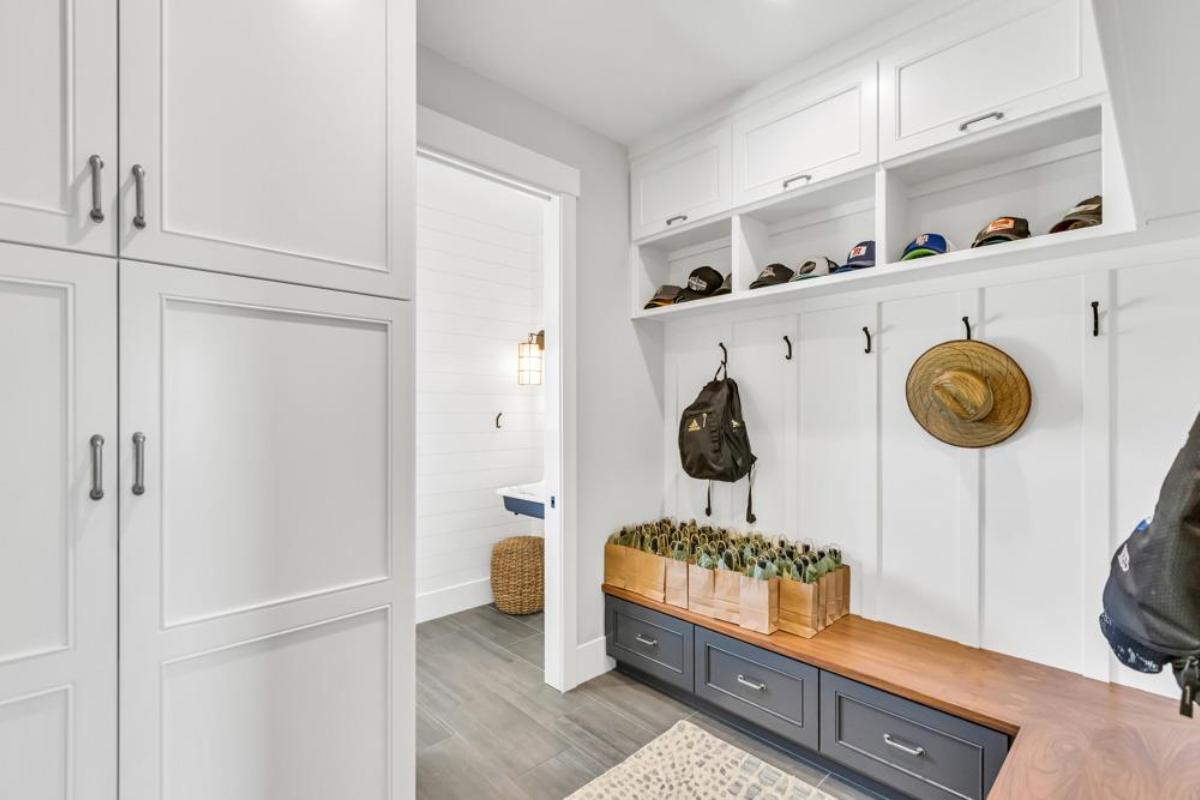 A mudroom featuring storage cabinets, a bench with bags, and hooks for hats and coats.