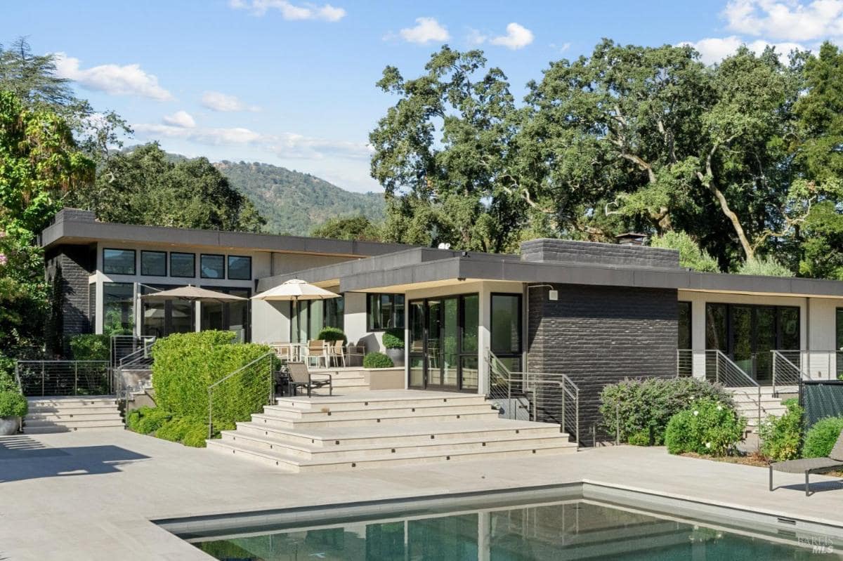 A back view of the house featuring steps, patio seating, and a swimming pool with surrounding greenery.