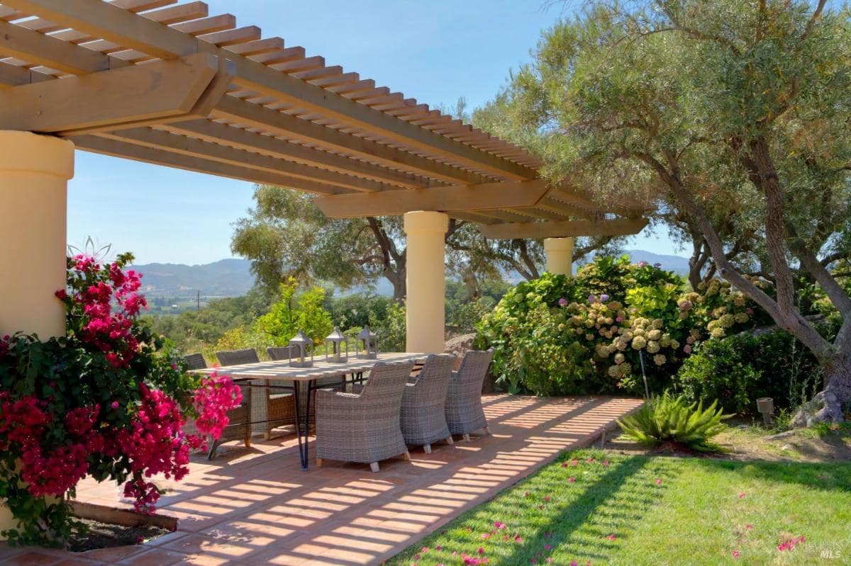 A pergola-covered dining area surrounded by greenery.