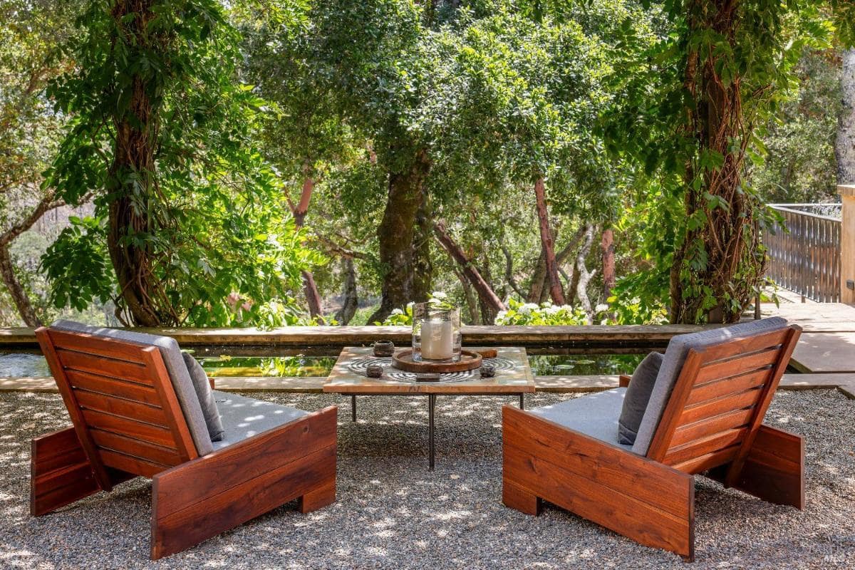 An outdoor seating area with two wooden chairs facing trees.