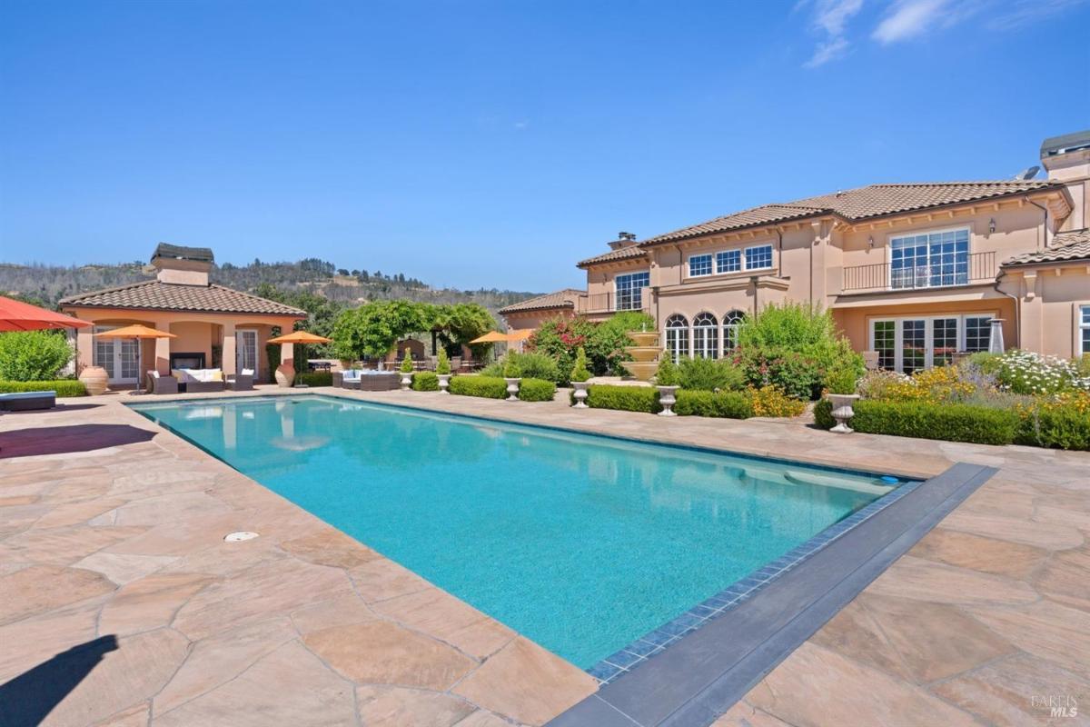 A large rectangular swimming pool is surrounded by stone paving, with the main house and a guest house nearby.