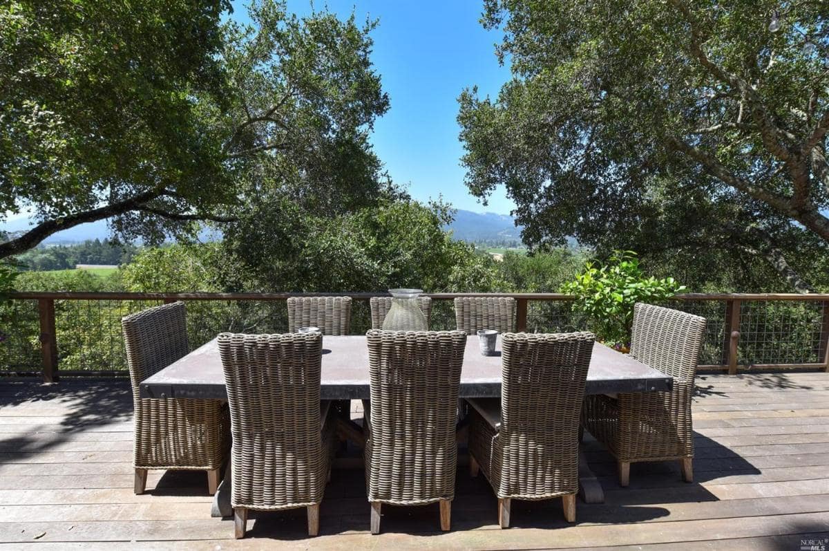 Outdoor dining area with a rectangular table and eight chairs surrounded by trees.