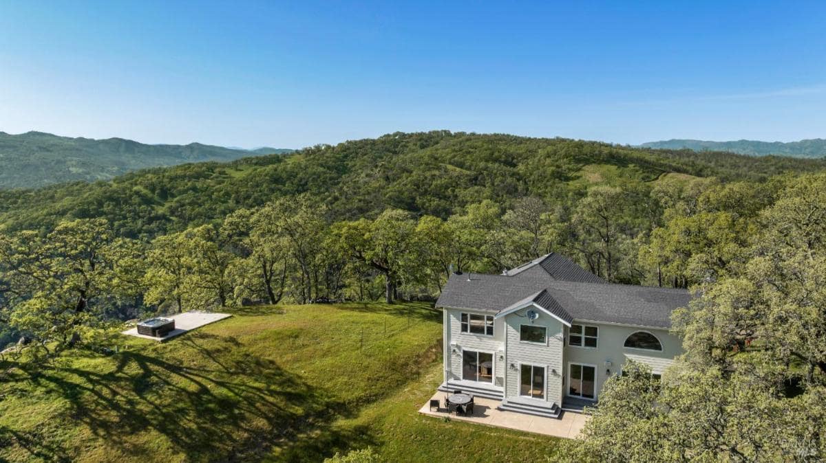 A large house on a hillside with a deck and trees surrounding it.