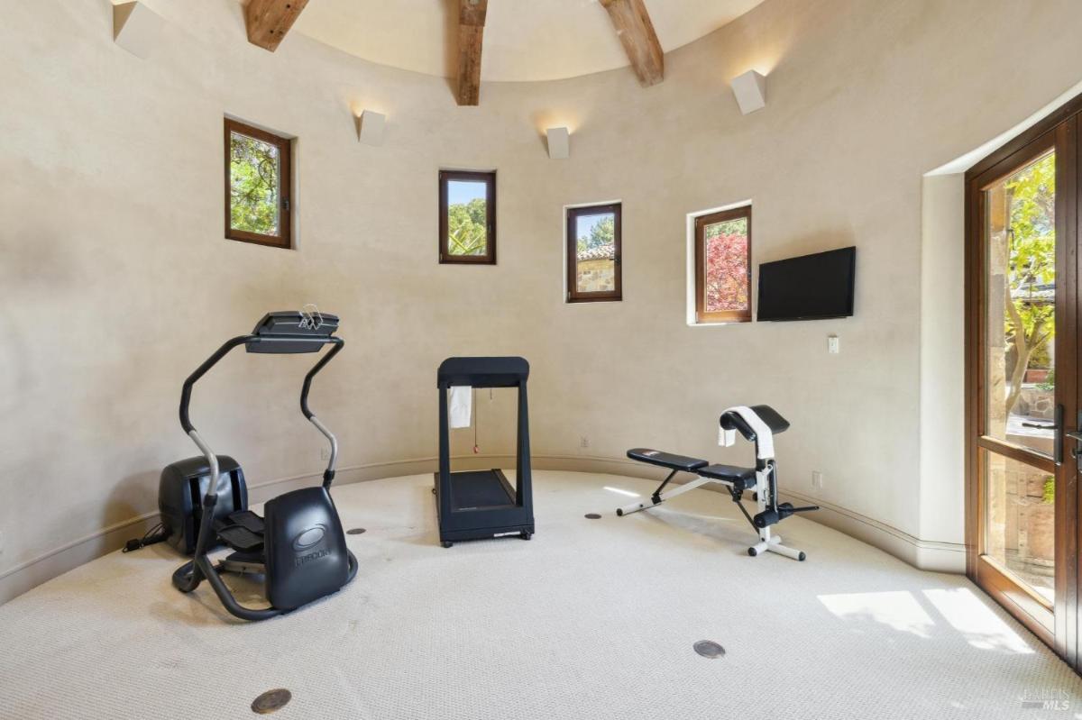 A home gym with curved walls, featuring a treadmill, an exercise bike, and a bench.