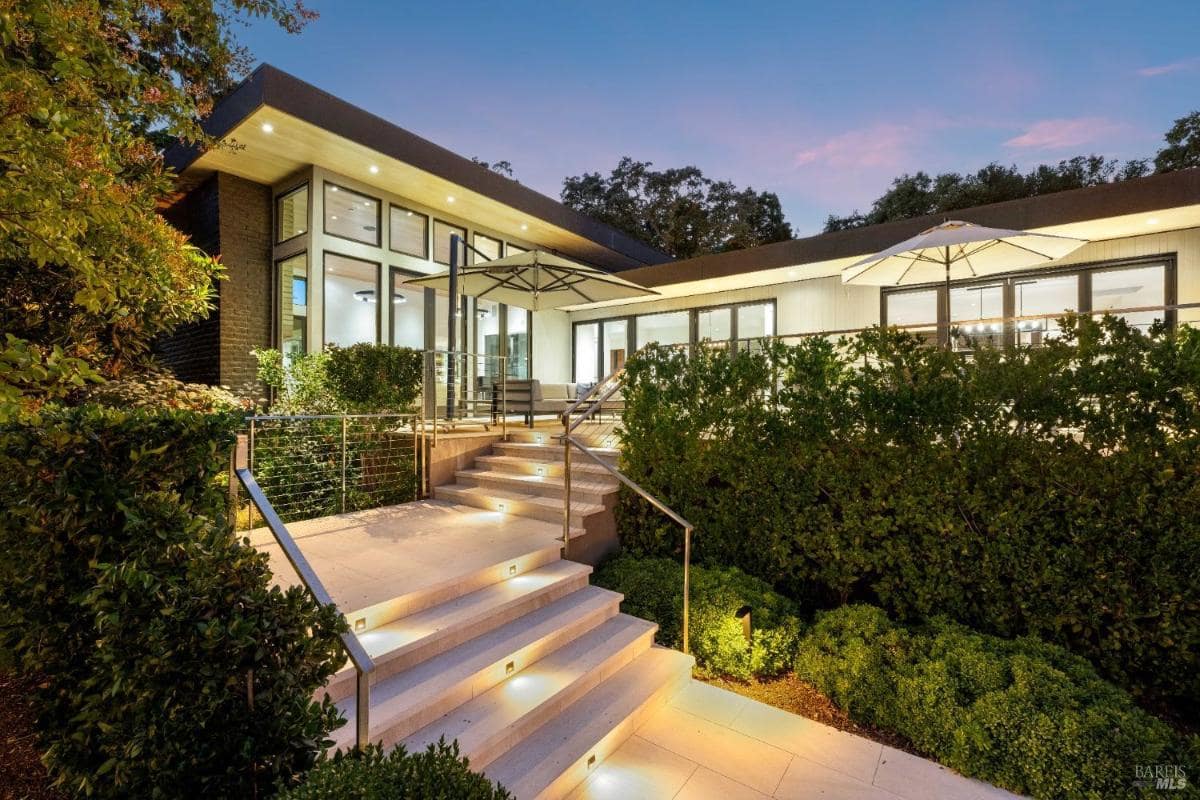  Outdoor stairs with built-in lights leading to a modern house, surrounded by landscaping and trees.