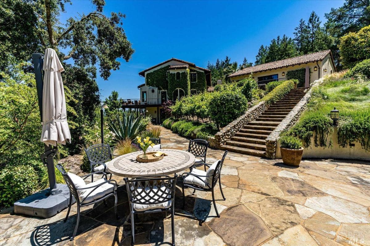 A landscaped patio area with a round table, umbrella, and steps leading to the house.