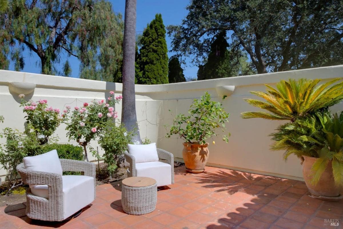 A courtyard with two chairs, plants, and terracotta flooring.